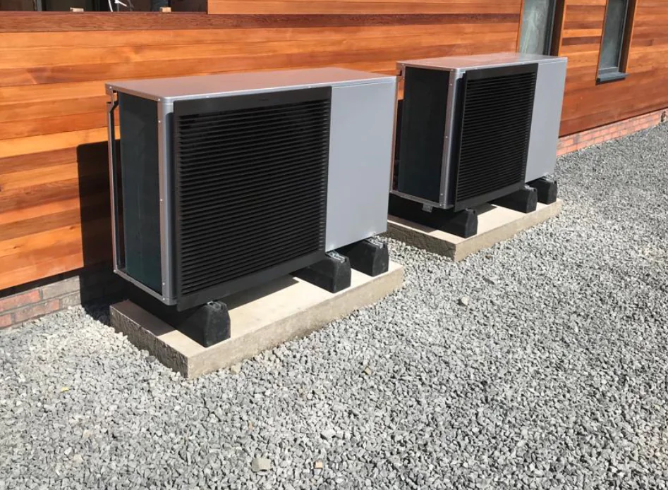 Outdoor heat pumps on gravel by house.