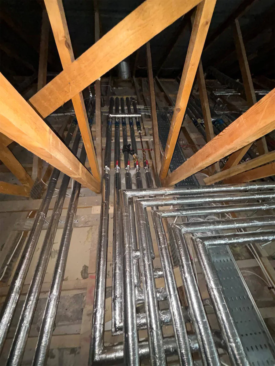 Insulated pipes in attic with wooden beams.